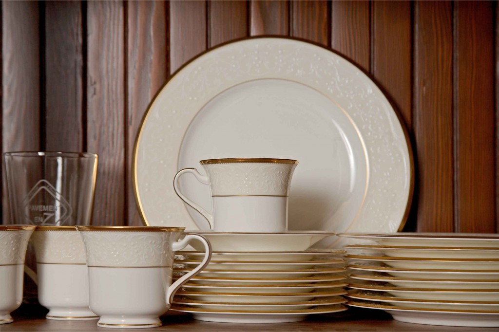 White china collection with gold rimming placed in a wooden cabinet with beadboard backing. 