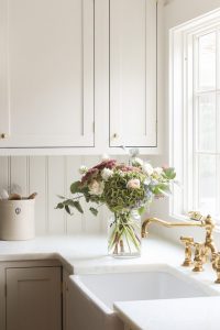 Beabdoard backsplash in an all white kitchen with brass accents and fresh flowers on the counter.