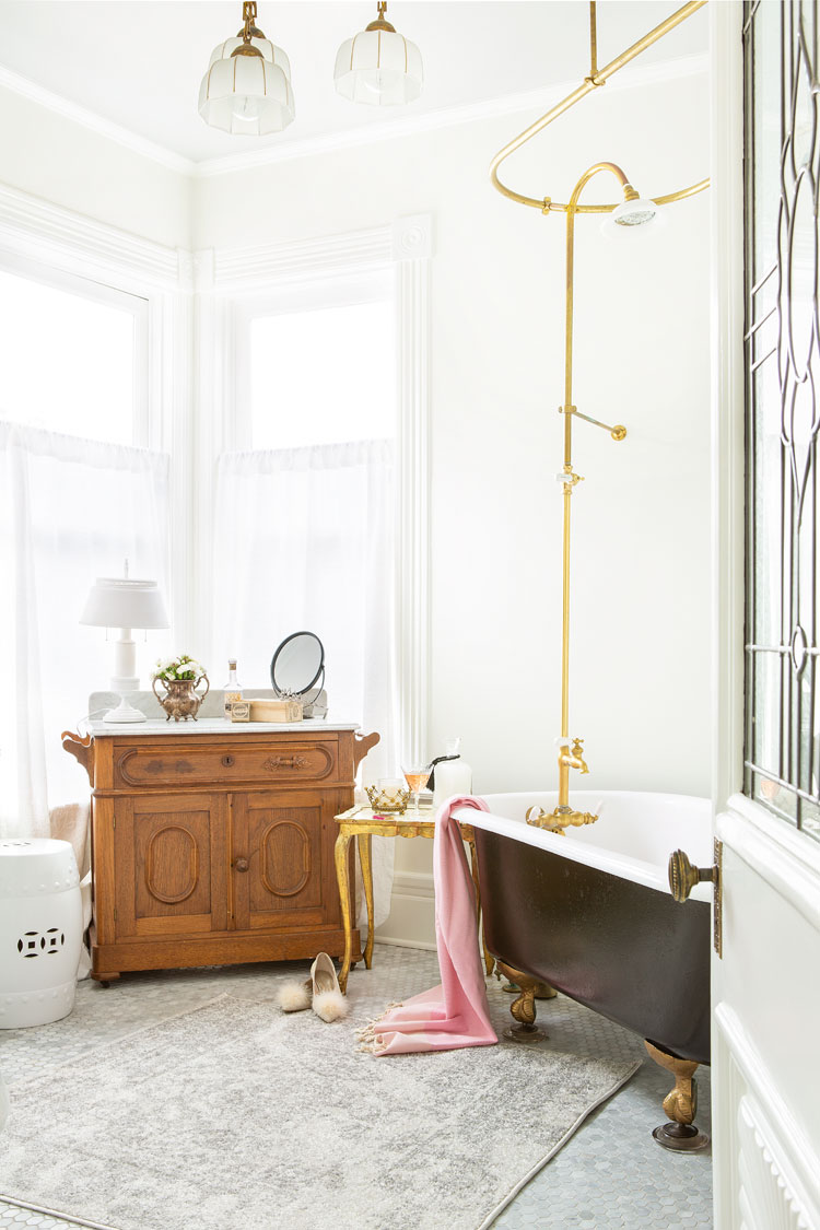 There are gold accents and dark claw-foot bath tub, a lovely large area rug and a small wooden cabinet that really pops out.