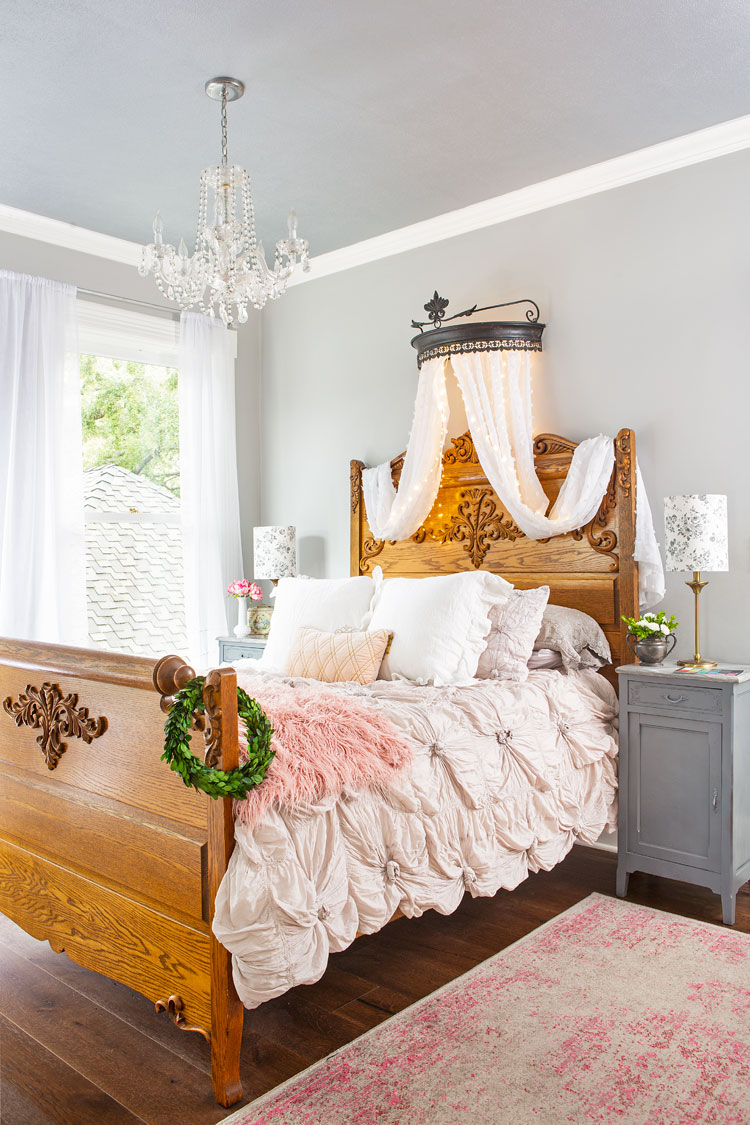 A grandiose high-rise wooden bed decorated with white and pink accents and under the bed a rug of the same color palette. 