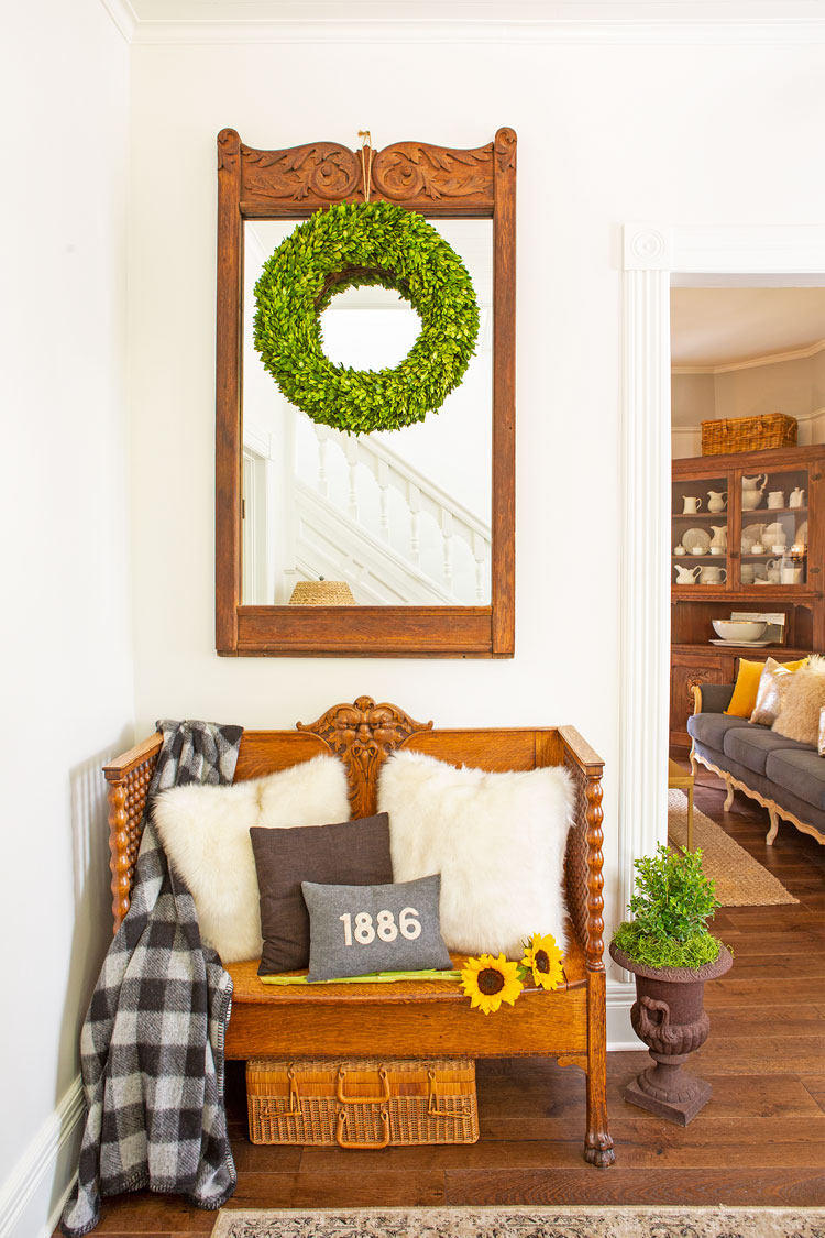The foyer has a cozy seating area with a small but ornate wooden bench placed under an antique wooden framed mirror. 