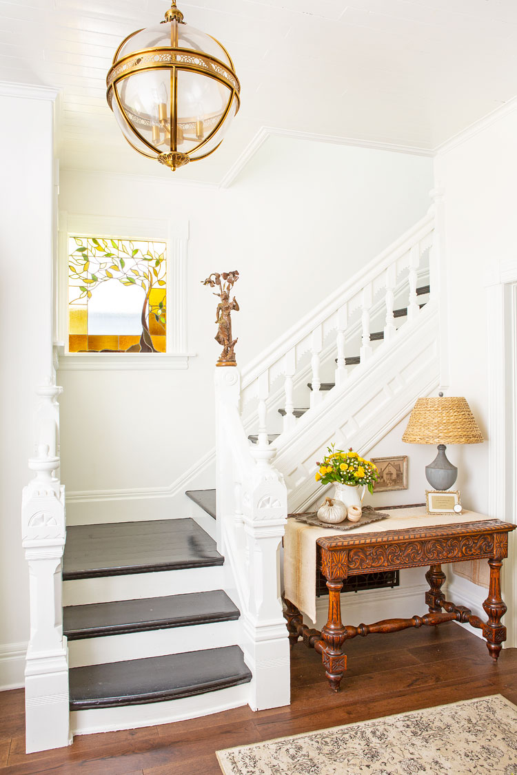 Regal staircase off of the entryway with an orb pendant hanging from above and a statement wooden table in the nook at the bottom of the stairs.