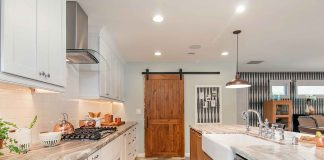 An open-space concept, galley kitchen with light paint colors and stainless steel appliances. The pantry has a custom barn door.