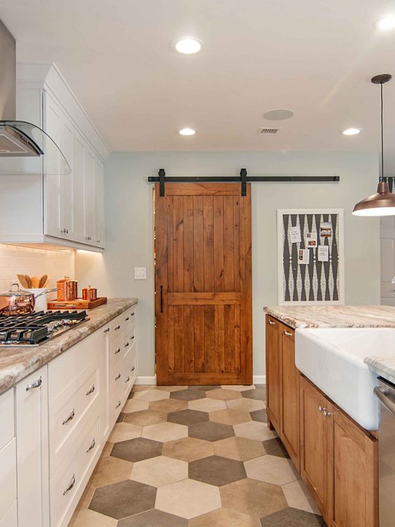 An open-space concept, galley kitchen with light paint colors and stainless steel appliances. The pantry has a custom barn door.