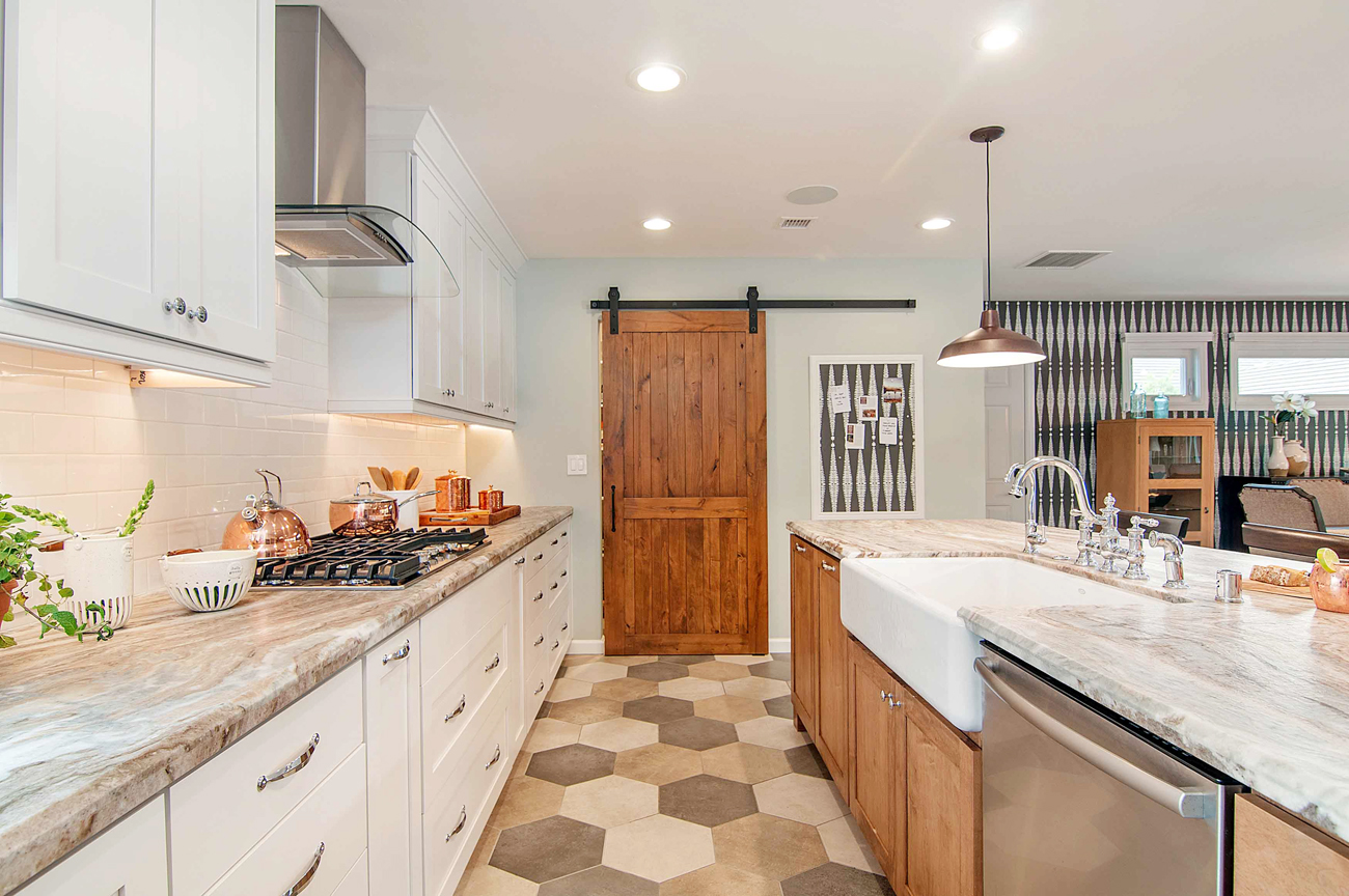 An open-space concept, galley kitchen with light paint colors and stainless steel appliances. The pantry has a custom barn door. 