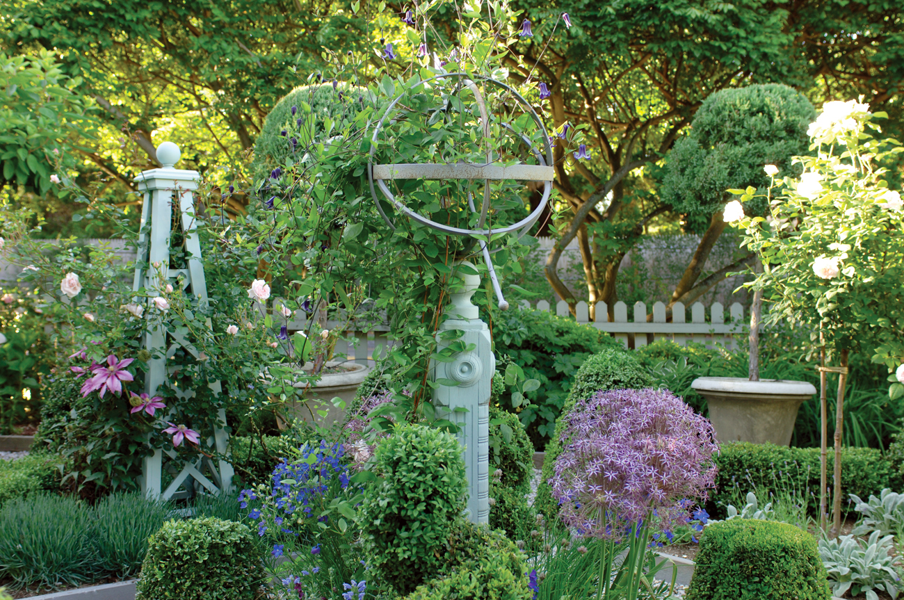 Lush green yard with neutral colored picket fence in the background and metal sculptures artistically placed on the grounds. 