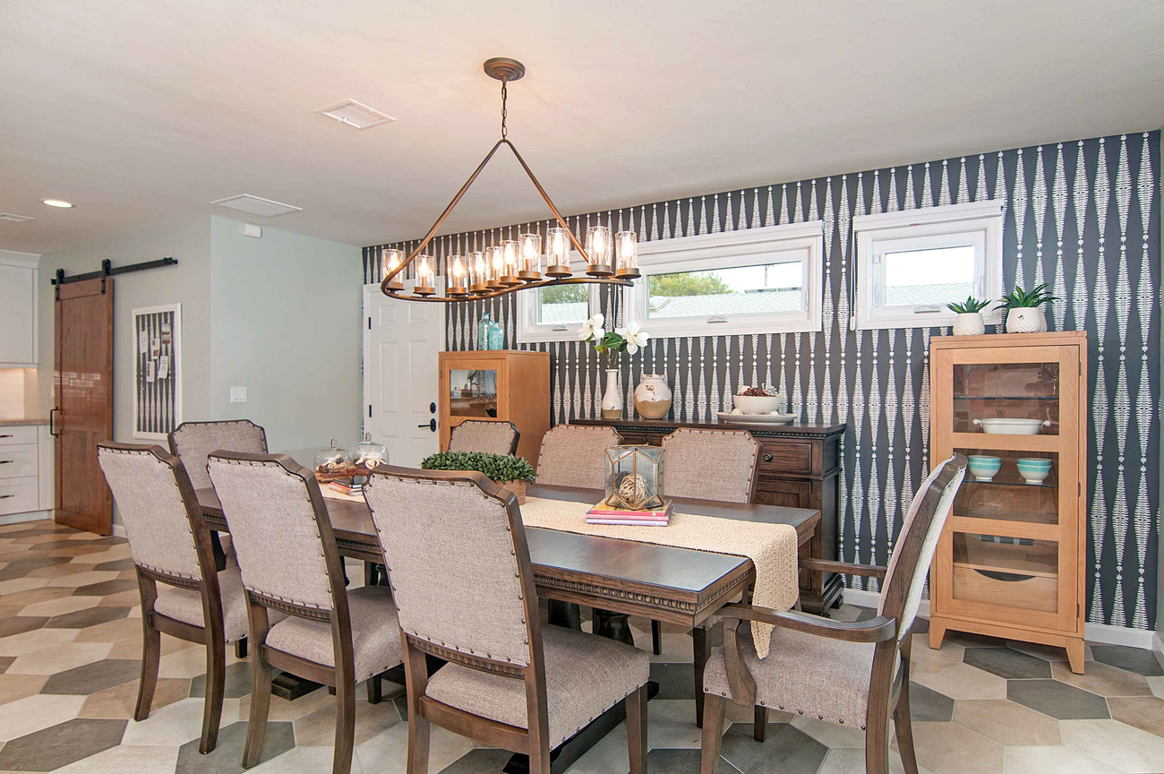 wallpapered dining room with wooden hutches and dining set, overlooking the open kitchen.