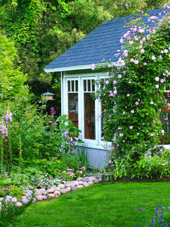 Vibrant green yard with a cottage style shed. The open shed door is welcoming and beautiful flowers grow up the side of the wall tying the shed into the yard.