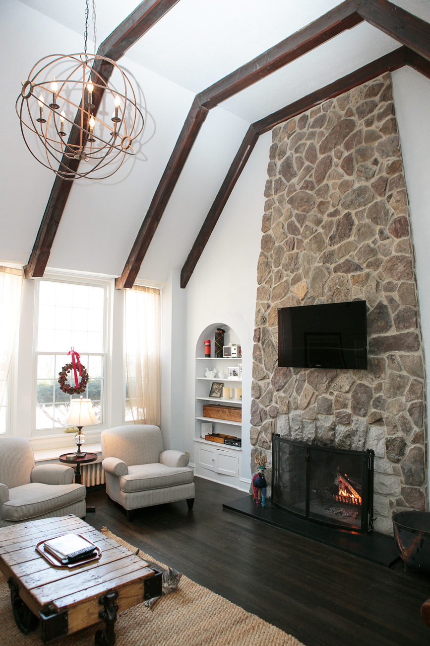 Cottage living area with stone fireplace that reaches up to the ceiling, which features exposed beans and a spherical light fixture.