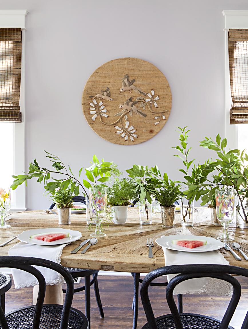 Rustic looking dining table topped with fresh greenery trimmings in vases. 