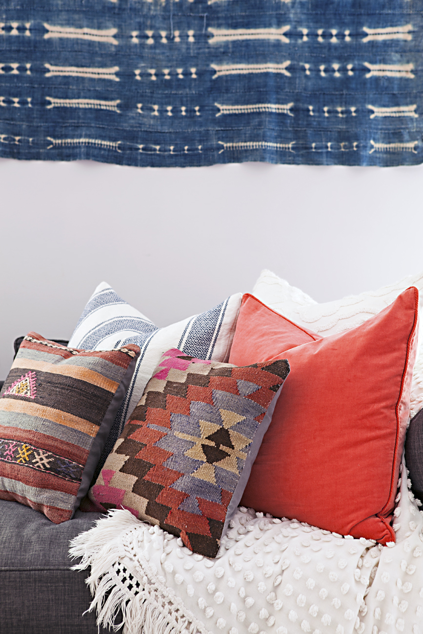 Vintage pillows arranged on a couch under a textile indigo mud cloth hanging.
