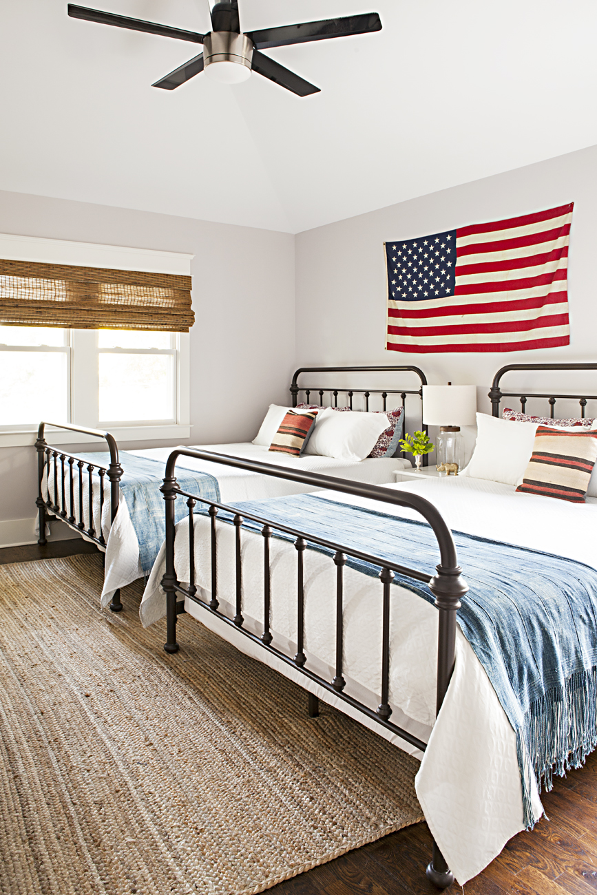 Americana guest bedroom with matching queen sized beds under a hanging American flag on the wall.