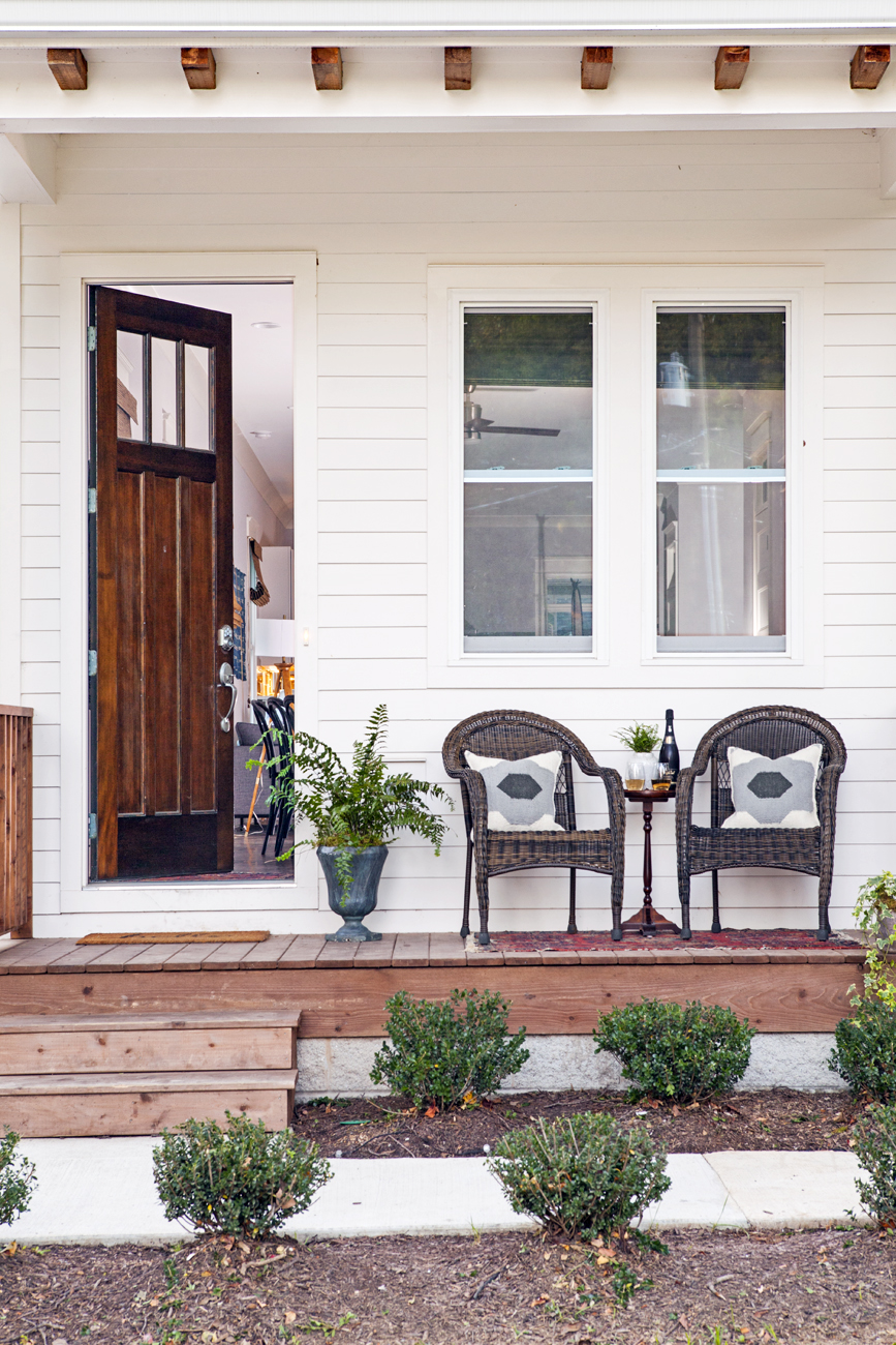 Wooden deck with whicker seating area and the front door open and inviting you into the home.