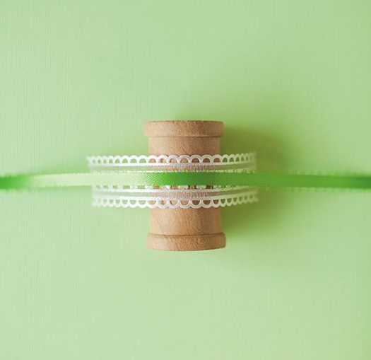 a layer of ribbon and trim are wrapped around a wooden spool to make an ornament