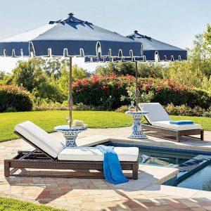 update your patio for spring with this blue patio umbrella with white piping over a cozy set of white pool -side lounge chairs with lush white cushions