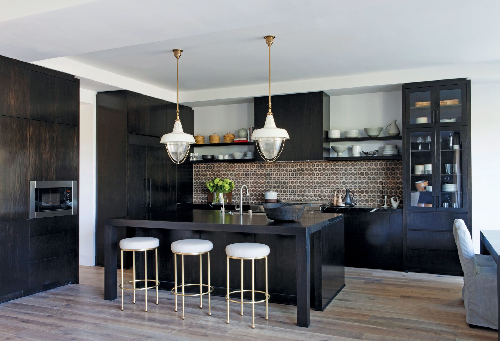 Black kitchen island with brown tile backsplash and overhead lights