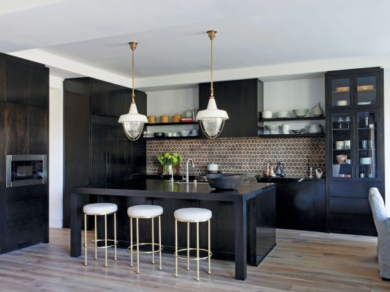 Black kitchen island with brown tile backsplash and overhead lights