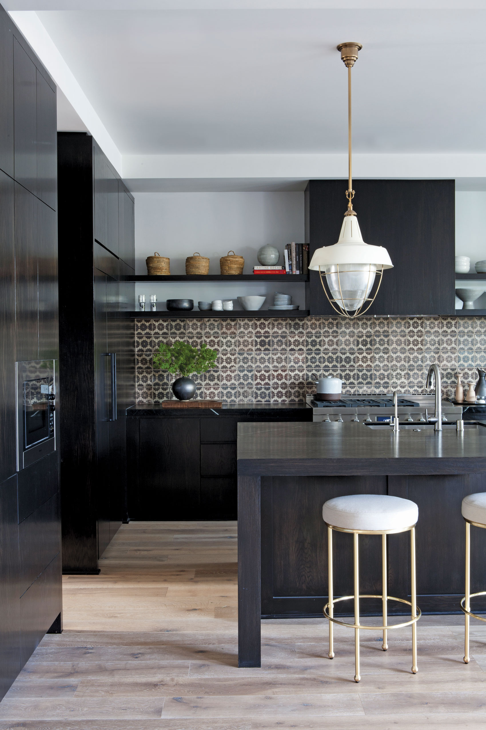 Light hardwood floors contrast black kitchen islands with tile backsplash