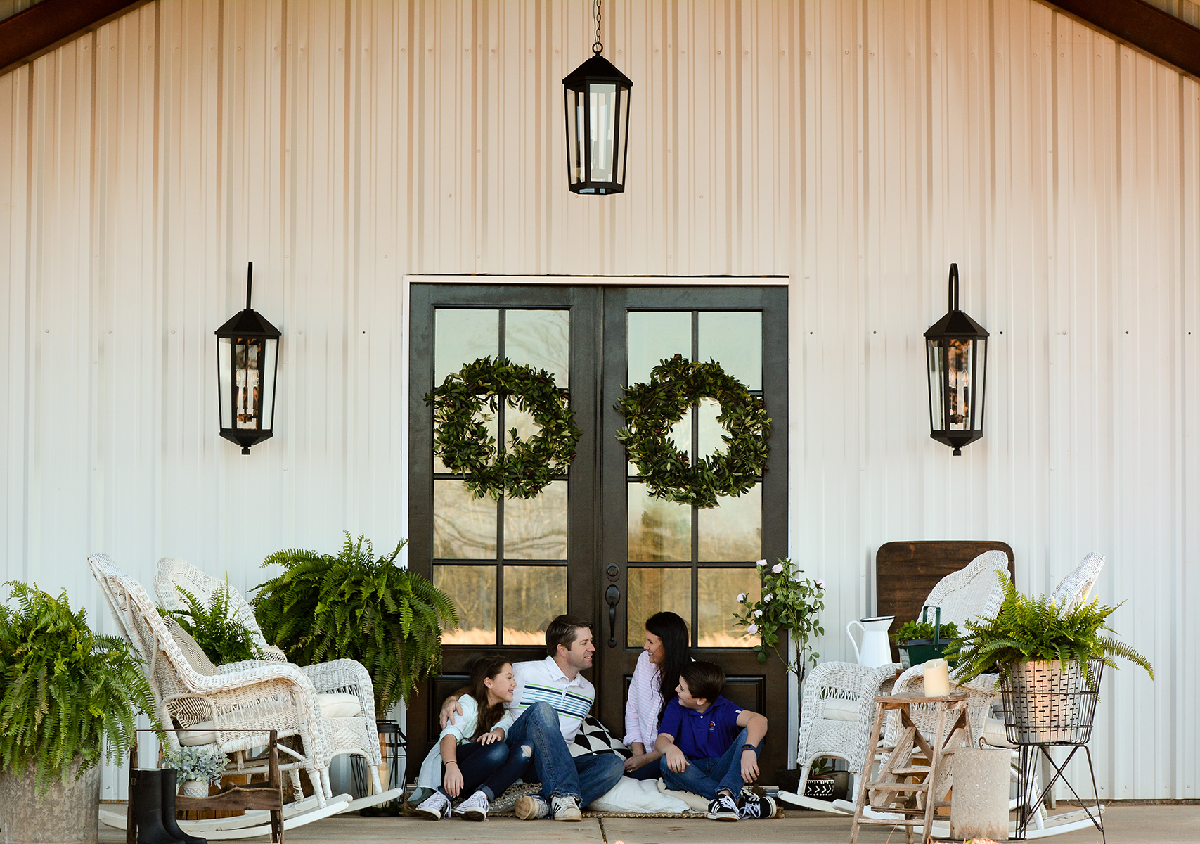 Porch Light Fixtures and White Farmhouse Home with a family sitting on the front porch.