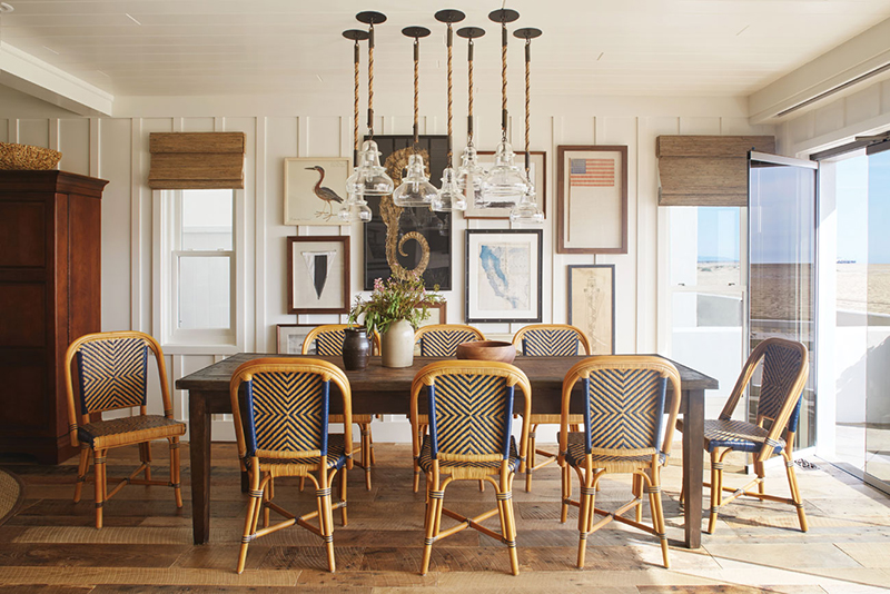 White and bright dining room with large wooden dining table, 7 hanging pendant lights and a collection of vintage art on the back wall. 