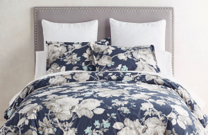 Navy blue and white floral duvet set shown with white pillows and a tufted gray headboard.