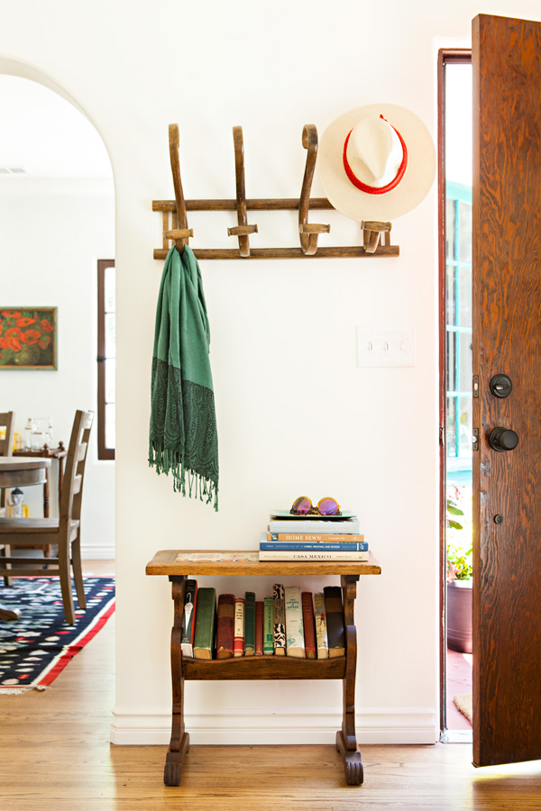 Spanish bungalow entryway with the wooden door cracked open and a small table and a hat rack.