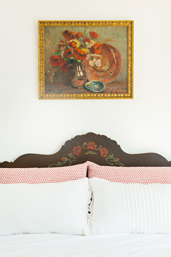 vintage paiting above an antique bed with painted detail and a gold frame.