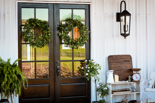 The front porch features elegant front doors that have been painted high-gloss black, which are complemented by the timeless lantern pendant by Capital Lighting. Lush wreaths from Balsam Hill warm up the entry with a dose of verdant green.