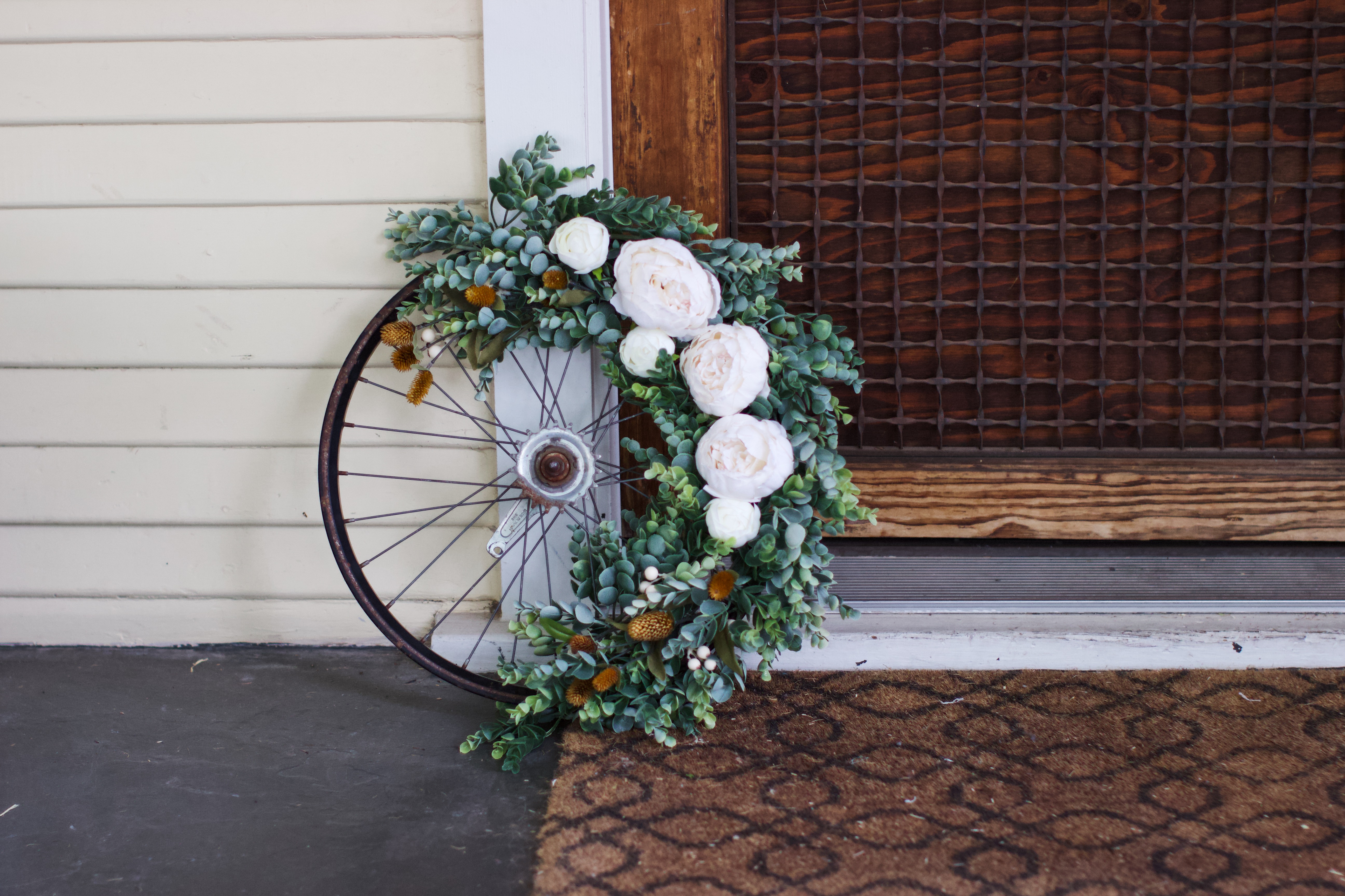 Round floral decorative bike wheel wreath with light pink flowers and greenery from Bloom Valley Market.