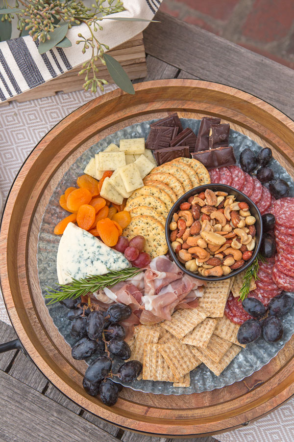 Here a zinc platter sits atop a wooden tray for a farmhouse chic look. Use complimentary herbs to section off different food items and bring a pop of green to your plate.