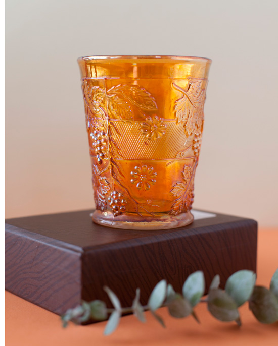 This carnival glass tumbler is by Indiana Glass and the pattern is called harvest grape in the amber marigold color.