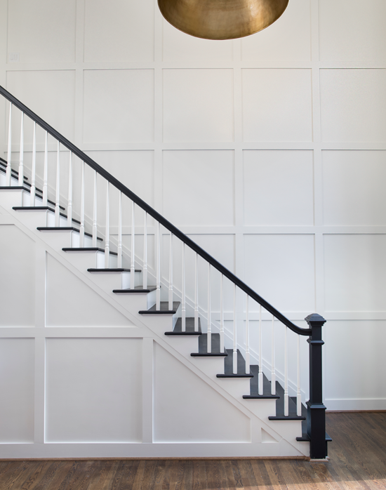 A staircase becomes a work of minimalist art, with the dark railing and steps contrasting against the white wainscoting.