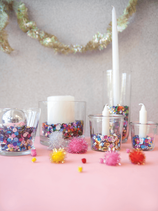 Sequin-filled glass tumblers topped with ornaments and candles.