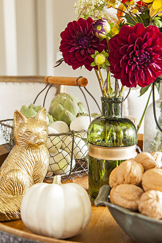 Centerpiece with bowl of walnuts, green vase of red dahlias, a golden fox and a white pumpkin. 