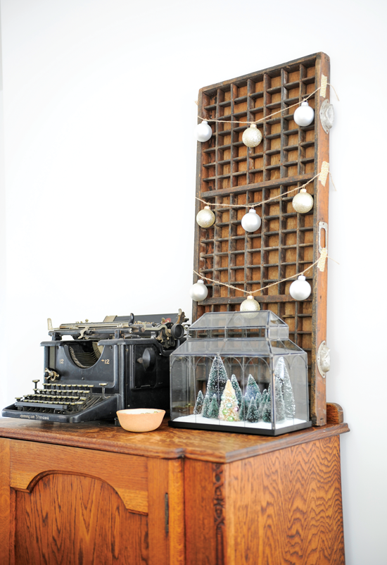 A printer’s tray is decorated with twine and ornaments, while a terrarium that usually holds succulents has bottlebrush trees in winter instead.