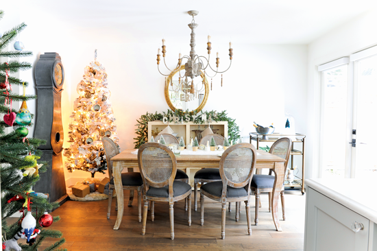 Dining room filled with French Christmas décor and a variety of textures, including greenery, rustic accents, a beaded chandelier and a patterned rug. // Cottages & Bungalows