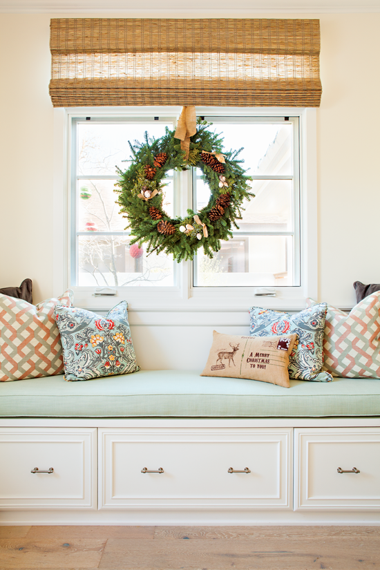 This custom-built window seat features a pinecone- and seashell-adorned wreath and mixed holiday pillows. // Cottages & Bungalows