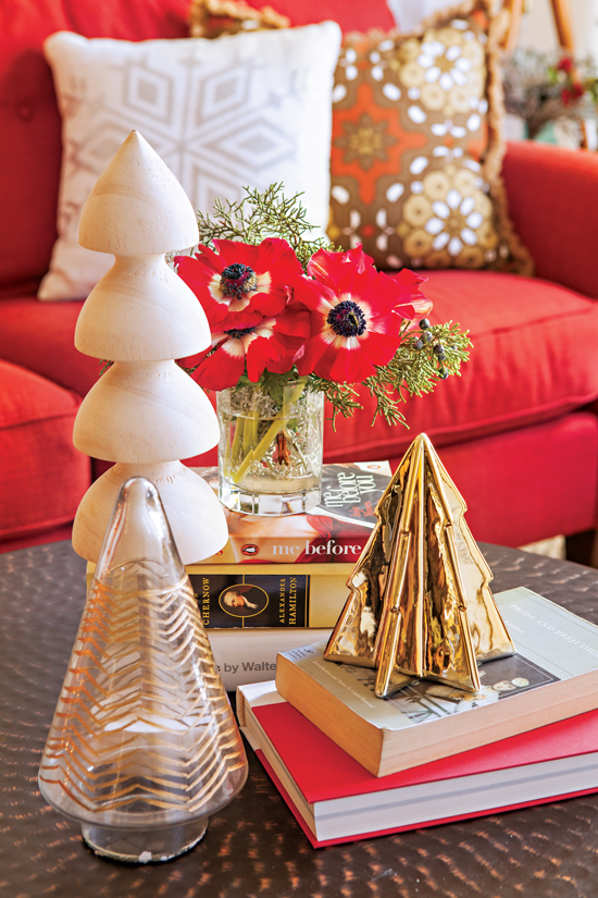 This stack of books serves as a landing pace for holiday décor, including small trees in a variety of materials and a vase of bright red anemones.