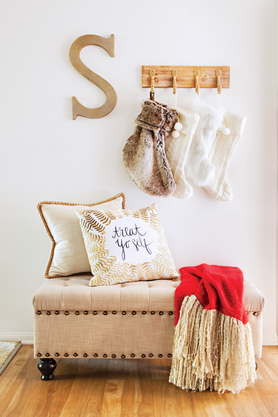 An entryway featuring an ottoman and throw pillows is transformed into a place to welcome Christmas guests. The scene is set with a red blanket and oh-so-fuzzy stockings.