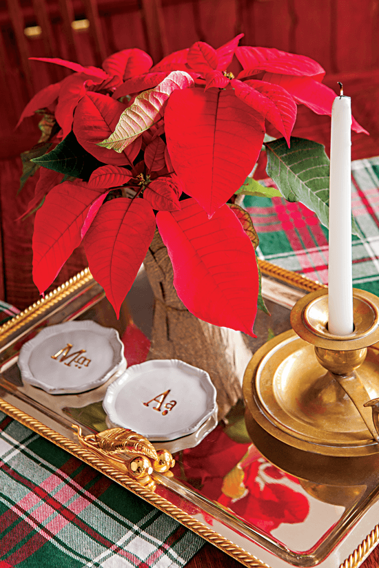 Tabletop display featuring a poinsettia, white monogramed plates and a candlestick arranged on a gold tray.