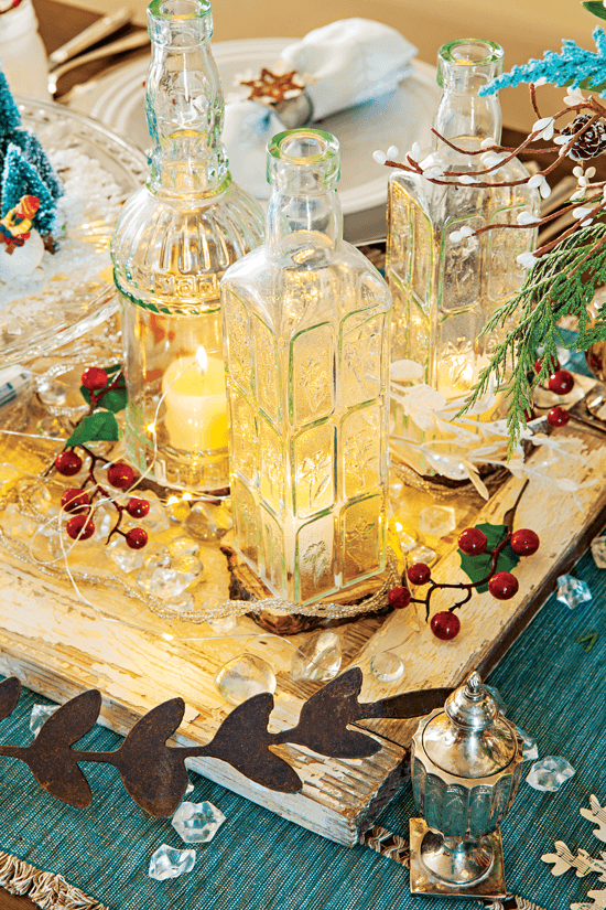 The centerpiece of the dining room table is layered with different colors and textures, including a blue table running, a rustic door-turned makeshift tray and repurposed bottles to serve as candle holders.