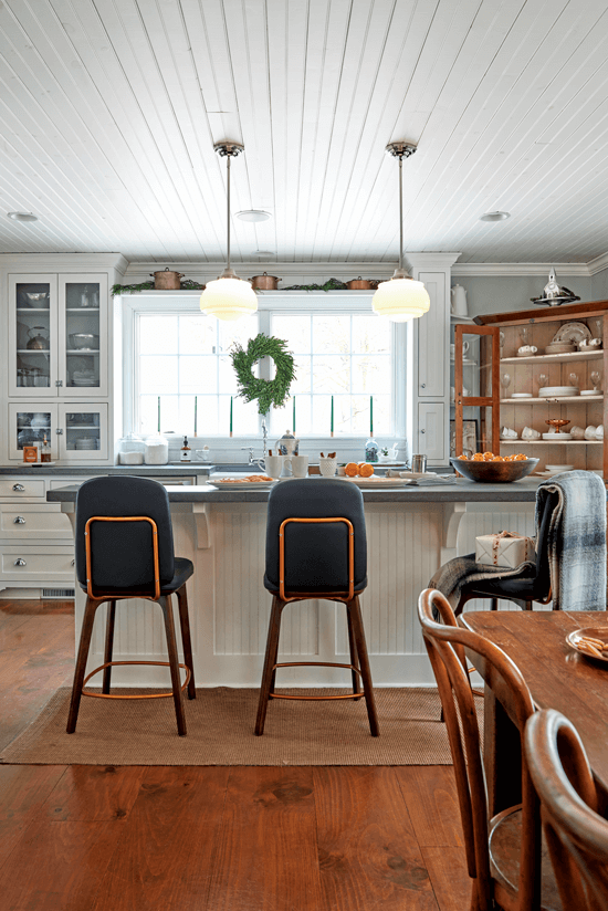 Navy barstools and a plaid blanket are placed at the island of this all-white kitchen, giving the light and bright space a cozy feel.