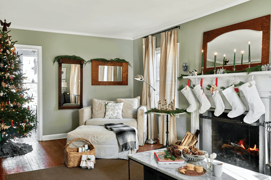 Cozy living room decorated with a Christmas tree and five white stockings hanging above the mantel. Live greenery is used to add pops of color and festivity.