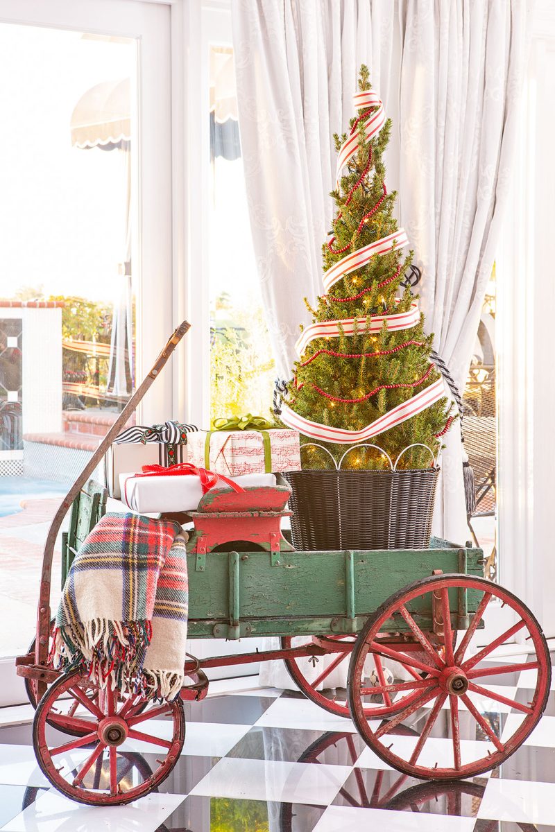 An antique, green wagon with a small tree, wrapped gifts and a tartan blanket in it