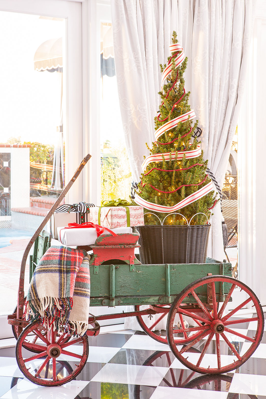 An antique, green wagon with a small tree, wrapped gifts and a tartan blanket in it