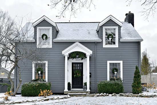 The snowy, grey exterior of this 1940 Cape Cod home is adorned with green wreaths and Granny Smith apples.