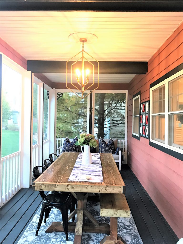 The updated cozy screened in porch from the Victory Farms project features a long farmhouse table and bench.