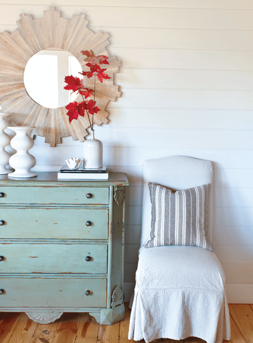 covered accent chair with decorative throw pillow alongside a distressed chest of drawers