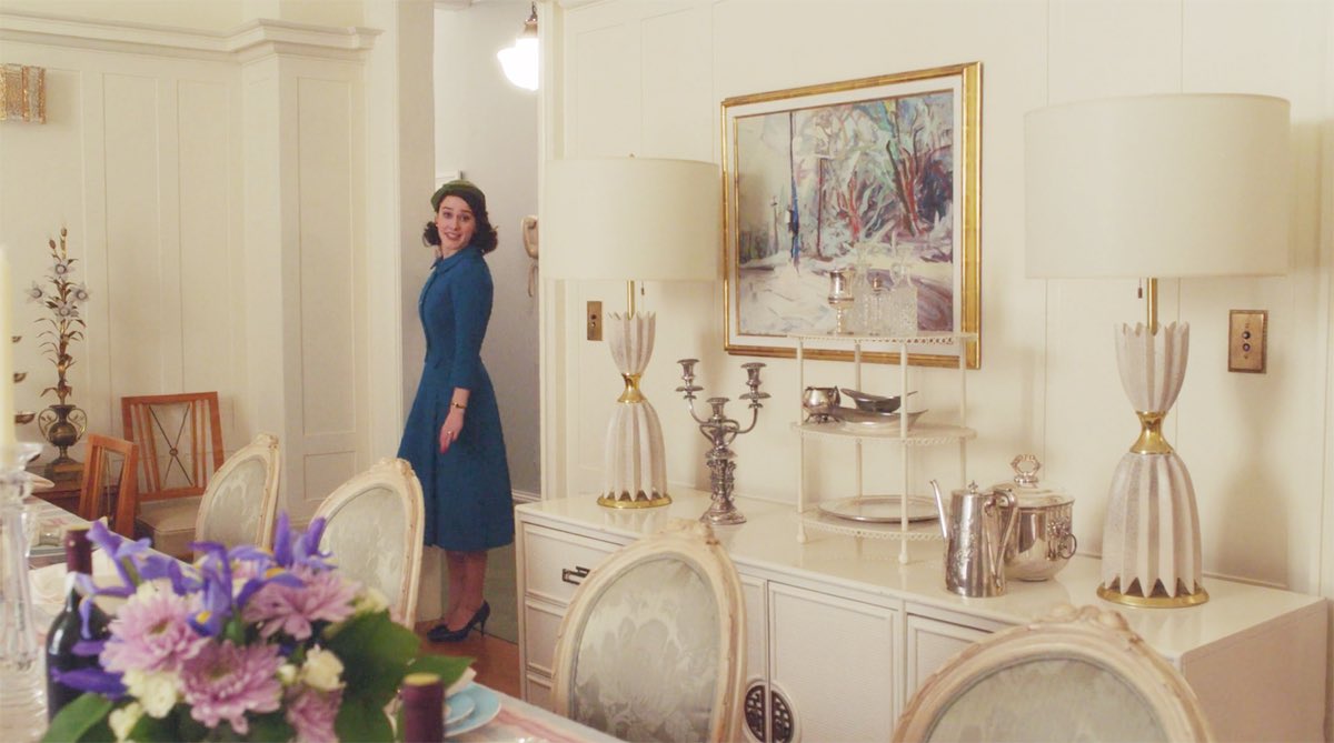 Mrs. Maisel standing in a elegantly set dining room.