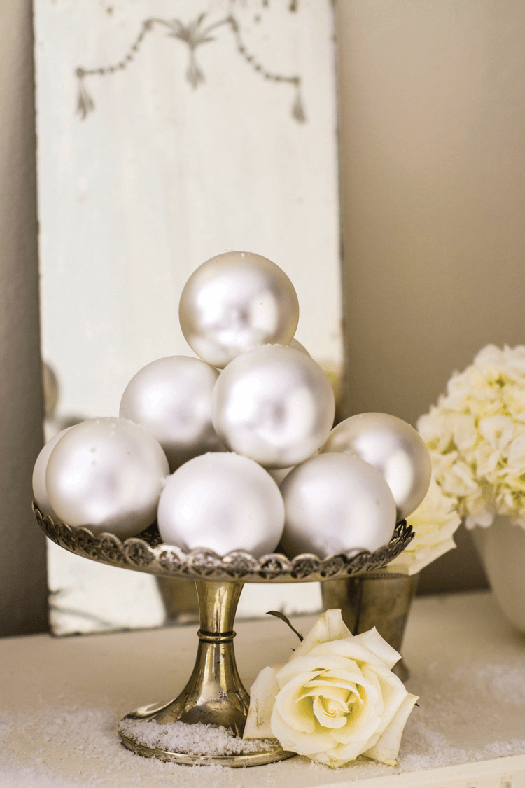 SILVER TRAYS AND COMPOTES can hold stacks of reflective Christmas balls, while vintage glasses and mint julep cups can display both fresh greens and lush white flowers.